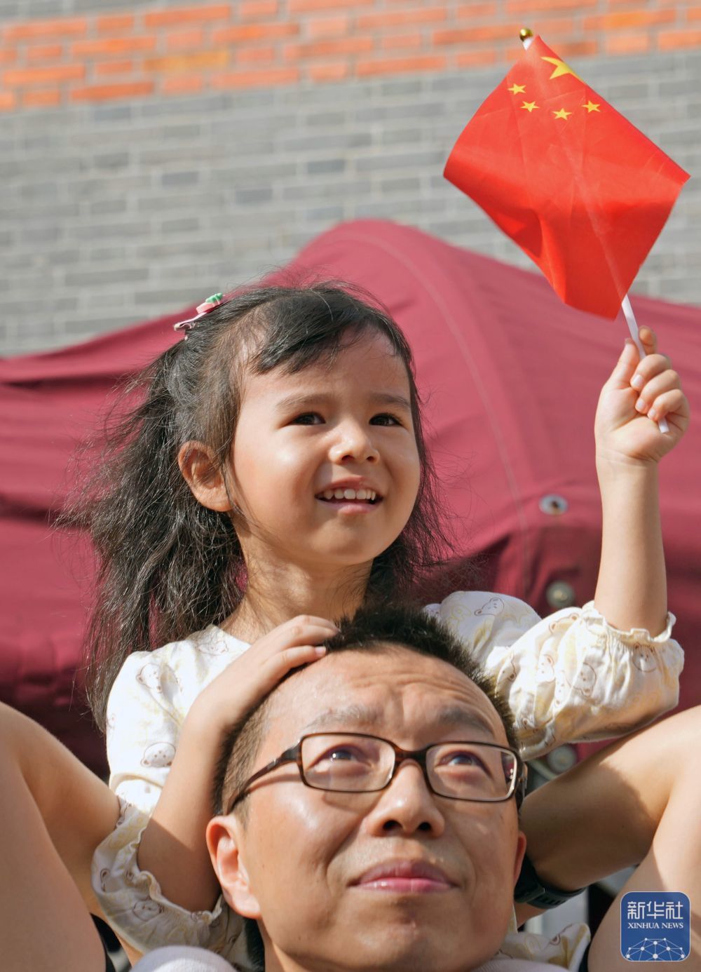 ↑ 10月1日，在上海中共一大纪念馆，一名小女孩坐在爸爸的肩膀上观看升旗。新华社记者 刘颖 摄