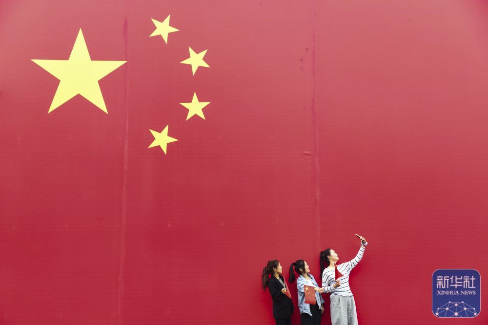 ↑ 10月1日，在河南省济源市那些年小镇，游客与国旗合影。新华社发（苗秋闹摄）